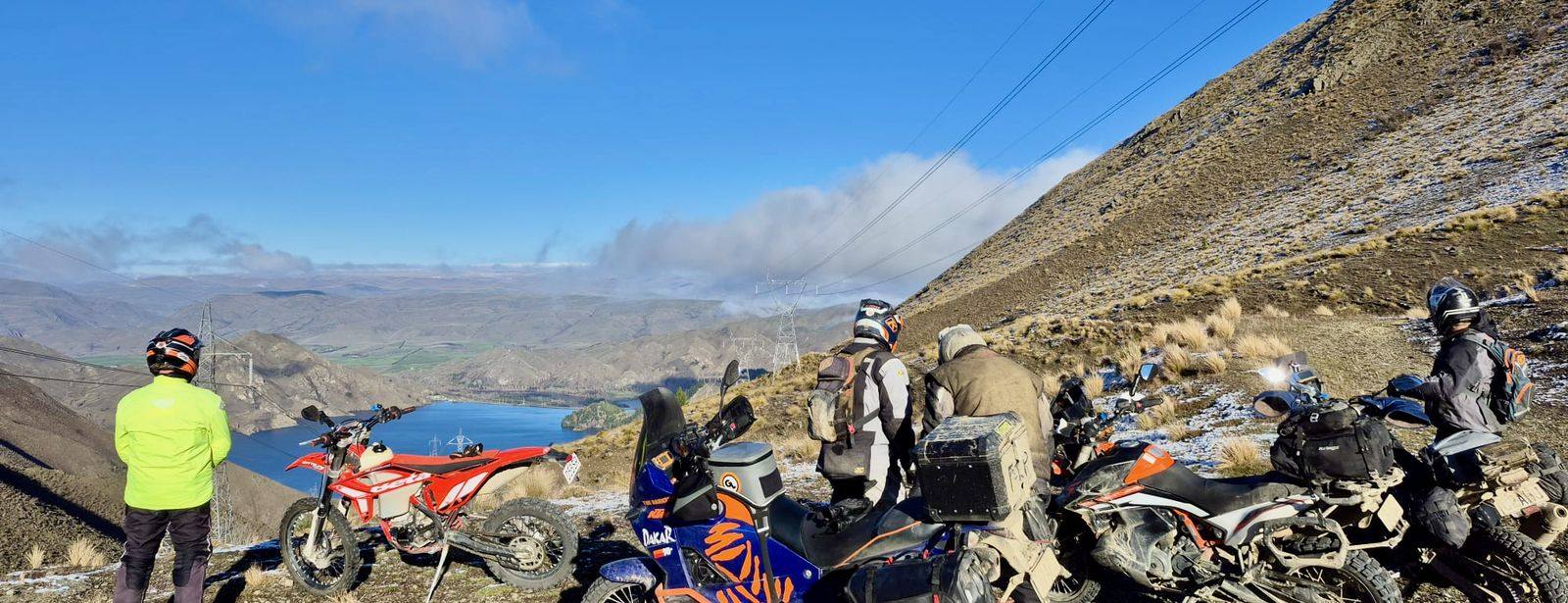 Adventure riders stopped high on a tussock ridge, looking out over a Waitaki lake
