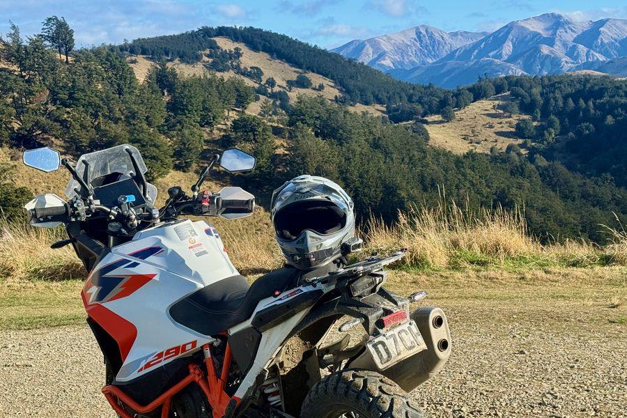 An adventure bike parked on a gravel road with snow-capped mountains behind
